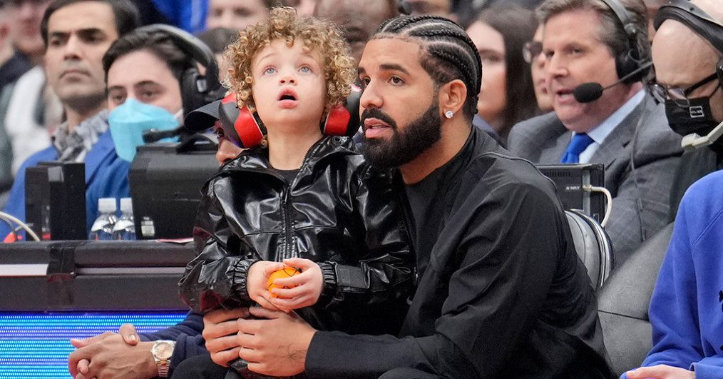Drake sits with his son Adonis while the Toronto Raptors play the Philadelphia 76ers